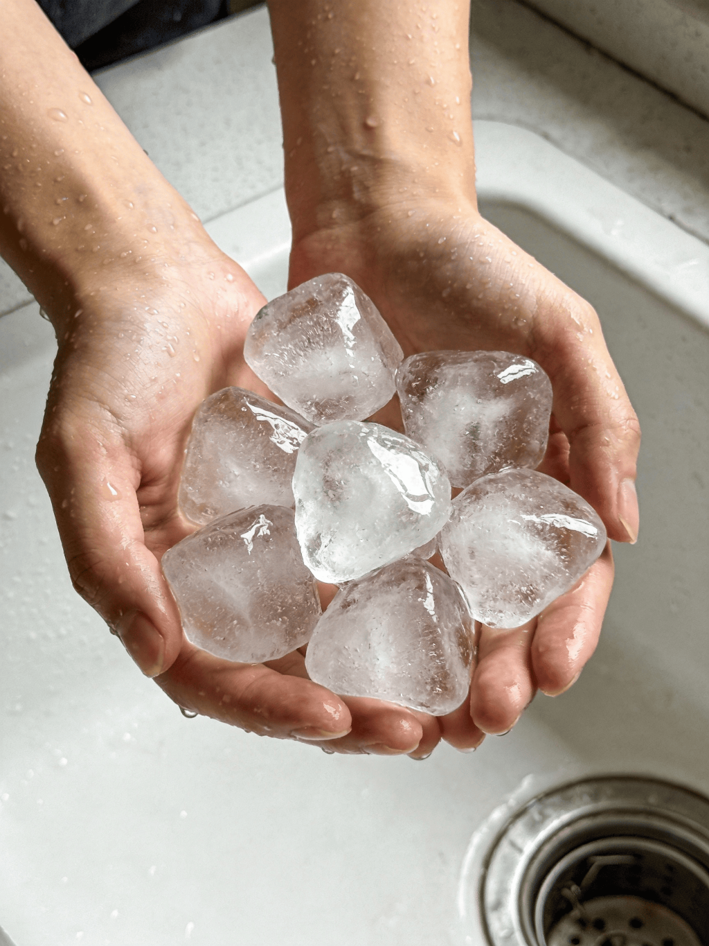 jimeng-2026-03-09-4777-雙手捧著7顆又大又透的不規(guī)則形狀的冰塊，背景白色廚房水槽，手被冰水打濕.png